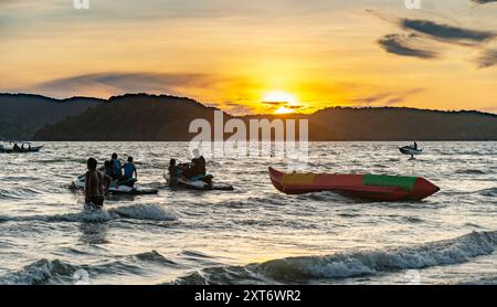 Langkawi Island, Malaisie-mai 01 2023 : le soleil se couche derrière les petites îles malaisiennes au-delà, et les jetskis jouent parmi les vagues tandis que les propriétaires apportent leurs bateaux Banque D'Images