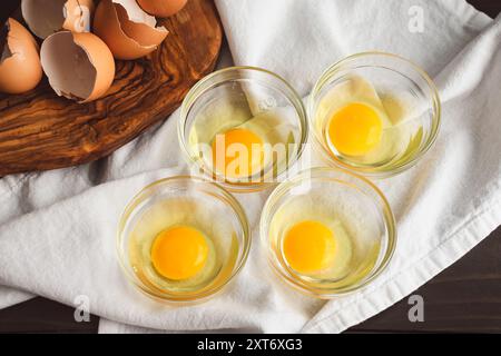 Oeufs craqués dans de petits bols en verre : oeufs crus craqués dans de petits bols de préparation en verre sur une table en bois rustique Banque D'Images