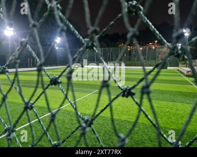 Terrain de football ou terrain avec gazon artificiel derrière la maille dans l'arène du complexe sportif dans la nuit. Banque D'Images