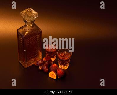 Liqueur de raisin-figue dans une carafe en cristal et deux verres à côté de fruits mûrs sur un fond brun. Gros plan. Banque D'Images