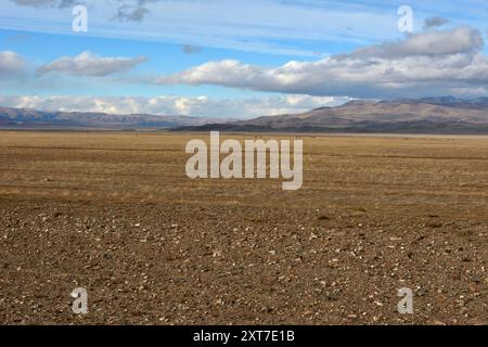 Une énorme steppe plate avec un éparpillement de petites pierres au pied d'une chaîne de montagnes un jour nuageux d'automne. Steppe de Chui, Altaï, Sibérie, Russie. Banque D'Images