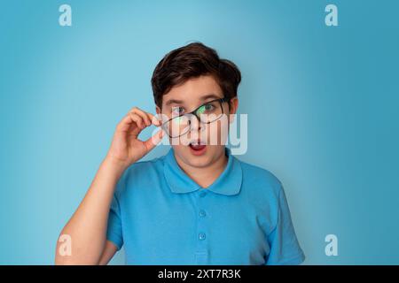 Un garçon surpris, beau, aux cheveux foncés, portant des lunettes à flancs écartés et un T-shirt bleu Banque D'Images