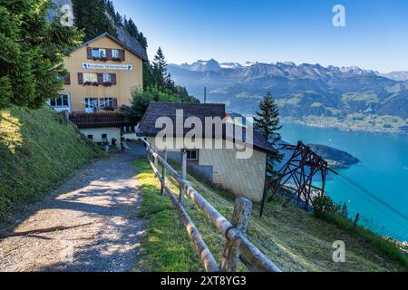 Le Berghaus Unterstetten peint en jaune, ses volets bordés de rouge, se dresse sur le flanc au-dessus du lac de Lucerne, un pylône de téléphérique s'élevant dans le cadre à droite. La vue s'étend brumeusement à travers le lac jusqu'aux chaînes de montagnes lointaines. Scheideggstrasse, Arth, Schwyz, Suisse. Banque D'Images