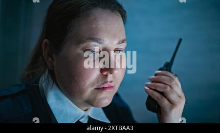 Gros plan d'un opérateur de sécurité féminin ou d'un répartiteur parlant dans un talkie-walkie et regardant des écrans assis sur le lieu de travail dans le centre de surveillance pendant le quart de nuit. Système de surveillance et de vidéosurveillance. Portrait. Banque D'Images