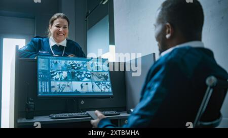 Afro-américain travailleur de la sécurité masculin assis sur le lieu de travail avec un moniteur d'ordinateur montrant des caméras de surveillance vidéo, utilise un téléphone portable. Garde féminine parle à un collègue, donne les clés. Système de vidéosurveillance. Banque D'Images