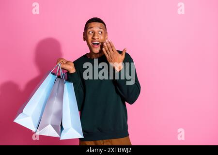 Photo de beau gars impressionné porter sweat-shirt tenant les acheteurs regardant l'espace emtpy isolé fond de couleur rose Banque D'Images