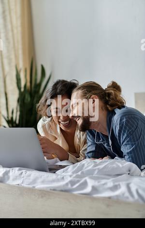 Un couple aimant se détend au lit, riant ensemble tout en naviguant sur Internet sur un ordinateur portable. Banque D'Images