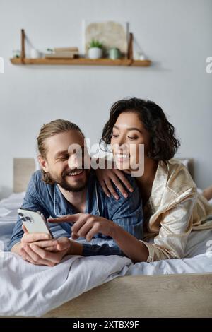 Au lit, un couple se détend : homme au téléphone, femme lui souriant. Banque D'Images