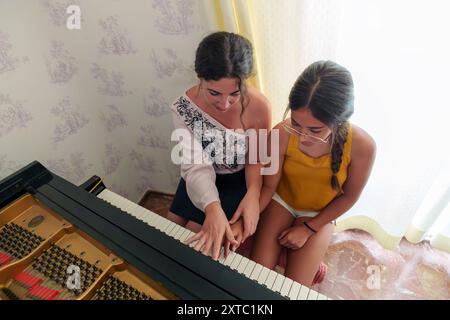 Femme hispanique dans ses 30 ans donnant des leçons de piano à une adolescente à la maison avec un piano à queue Banque D'Images