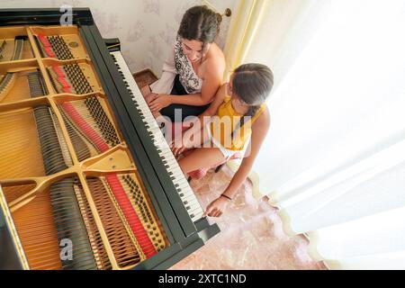 Femme hispanique dans ses 30 ans donnant des leçons de piano à une adolescente à la maison avec un piano à queue Banque D'Images