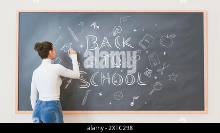 Enseignante écrivant "retour à l'école" sur un tableau noir dans une salle de classe. Le tableau noir est rempli de griffonnages liés à l'éducation. Rentrée scolaire et Banque D'Images