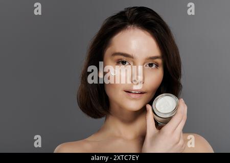 Une femme à la peau impeccable tient un pot de crème hydratante, mettant en valeur une beauté fraîche et confiante. Banque D'Images