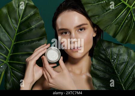 Une femme pose avec un pot de crème devant un fond vert éclatant. Banque D'Images