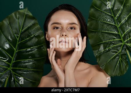 Une femme pose devant un fond vert éclatant, touchant son visage avec des mains délicates. Banque D'Images