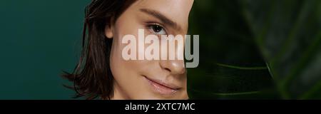 Un visage de femme est partiellement obscurci par une grande feuille verte. Banque D'Images