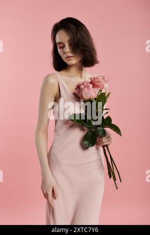 Une femme dans une robe rose tient un bouquet de roses devant un fond rose. Banque D'Images