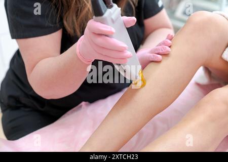 Une femme se fait épiler les jambes par une femme. La femme porte une chemise noire et la femme porte des gants Banque D'Images