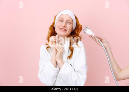 Une femme se fait coiffer avec un sèche-cheveux. Elle porte une robe blanche et un bandeau blanc Banque D'Images