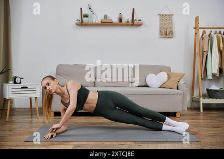 Une jeune femme effectue un exercice de planche latérale sur un tapis de yoga dans son salon. Banque D'Images