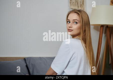 Une jeune femme aux longs cheveux blonds se détend sur un canapé chez elle. Banque D'Images