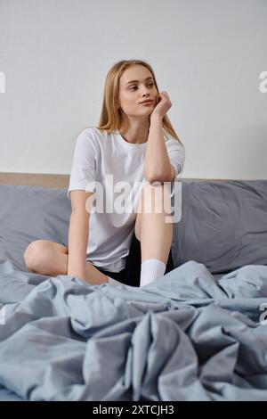 Femme assise sur le lit, regardant au loin, baignée de lumière du matin. Banque D'Images