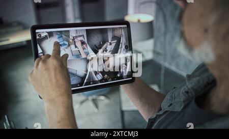 Technicien mature masculin regarde et contrôle les caméras de vidéosurveillance dans le bureau moderne à l'aide d'un ordinateur tablette. L'écran de la tablette affiche les images des caméras de sécurité. Surveillance et suivi. Système de surveillance et confidentialité. Banque D'Images