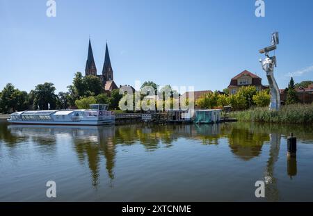 Neuruppin, Allemagne. 12 août 2024. Vue sur la promenade au bord du lac Ruppin avec l'église du monastère de composés Trinitatis (l) et l'objet d'art Parzival am See (R). Crédit : Monika Skolimowska/dpa/Alamy Live News Banque D'Images