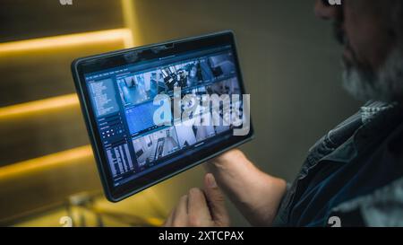 Technicien masculin surveille et contrôle les caméras de surveillance dans le bureau moderne à l'aide d'un ordinateur tablette. L'écran de la tablette affiche les enregistrements des caméras de vidéosurveillance. Surveillance et suivi. Système de sécurité et confidentialité Banque D'Images