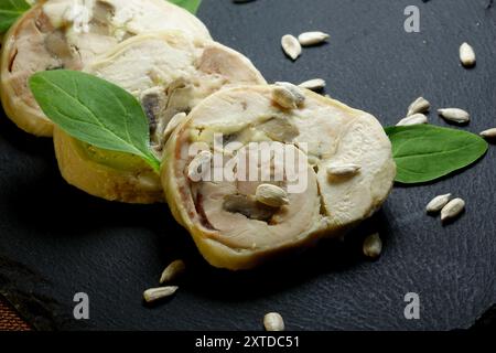 Le rouleau de viande tranchée est magnifiquement présenté sur un panneau de céramique noir, garni de feuilles d'épinards frais et de graines de tournesol. Banque D'Images