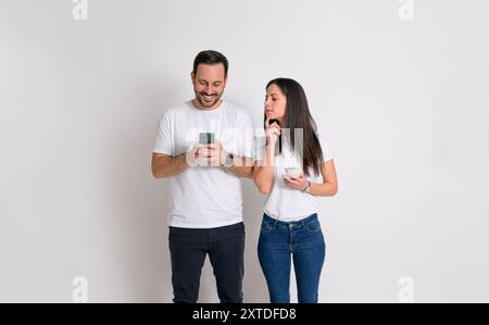 Femme curieuse regardant dans le téléphone de petit ami et essayant de vérifier ses messages sur fond blanc Banque D'Images