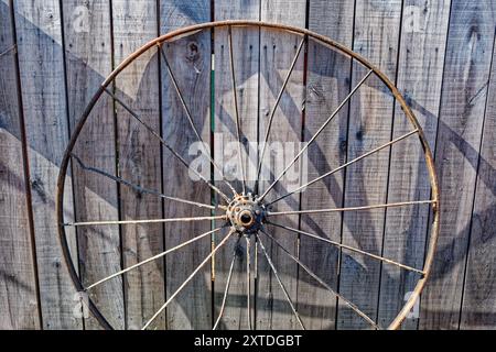 Roue de wagon en métal rouillé antique appuyée contre le mur de grange en bois à l'extérieur par une journée ensoleillée brillante Banque D'Images