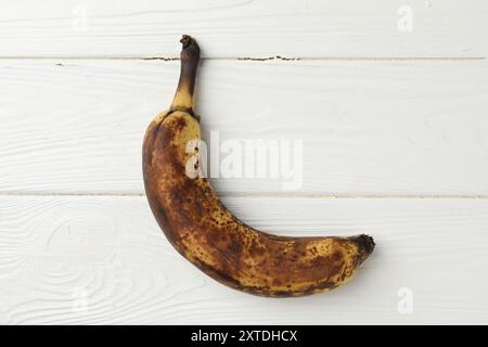 Banane surmûre avec des taches sombres sur la table en bois blanc, vue de dessus Banque D'Images