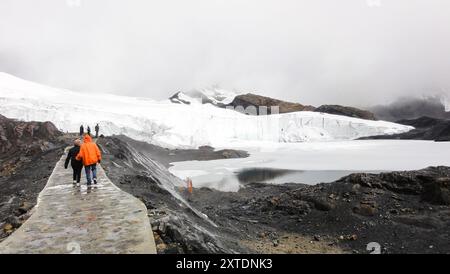 Touristes s'éloignant de la caméra sur un chemin près d'un glacier avec des montagnes en arrière-plan Banque D'Images