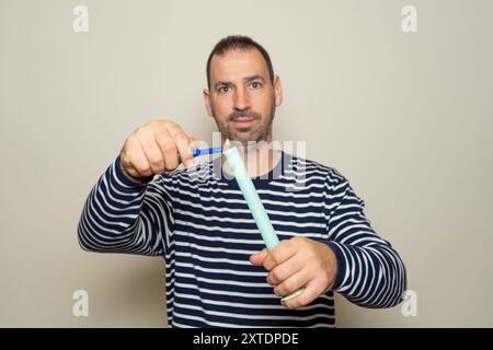 Homme hispanique barbu dans les années 40 vêtu d'un pull rayé allumant une bougie de cire allongée avec un briquet, isolé sur fond beige Banque D'Images