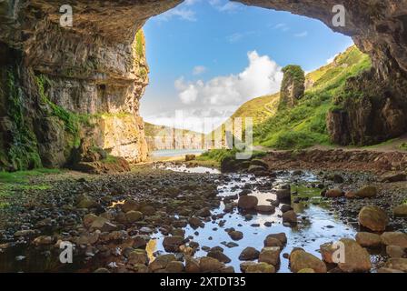 Découvrez le paysage captivant de Smoo Cave dans les Highlands, où les falaises de calcaire rencontrent des eaux sereines et une végétation luxuriante. Banque D'Images