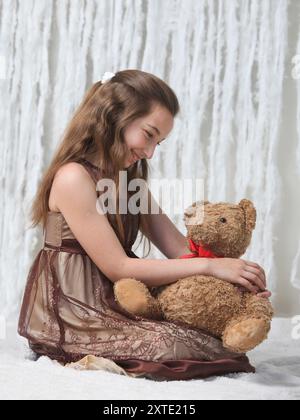 fille preteen mignonne dans une robe élégante avec ours en peluche sur fond clair Banque D'Images