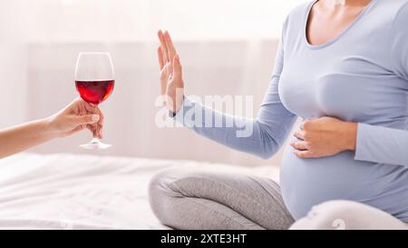 Méconnaissable fille enceinte refusant de prendre Wine Sitting on Bed Banque D'Images