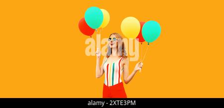 Portrait d'été d'une jeune femme souriante heureuse avec un tas de ballons jaunes rouges colorés s'amusant en portant un short, un t-shirt rayé, des lunettes de soleil sur oran Banque D'Images