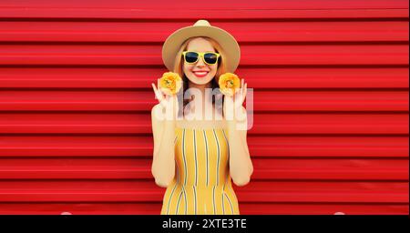 Portrait d'été d'une jeune femme souriante heureuse avec des boutons de fleurs dans un chapeau de paille rond sur fond rouge Banque D'Images