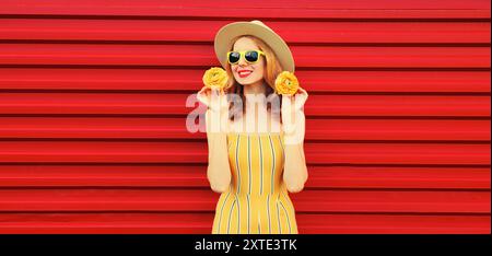 Portrait d'été d'une jeune femme souriante heureuse avec des boutons de fleurs dans un chapeau de paille rond sur fond rouge Banque D'Images