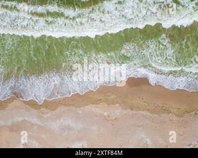 Vue aérienne des vagues de l'océan qui s'écrasent sur une plage de sable, créant un beau contraste entre l'eau vert émeraude et le sable chaud et texturé. A Banque D'Images