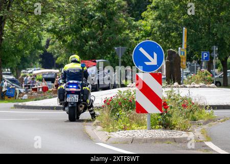 Une moto de police allemande avec des feux clignotants est vue sur un rond-point, avec des arbres verts en arrière-plan. Un panneau de direction indiquant la droite Banque D'Images