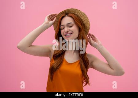 Jolie jeune femme flirty dans le chapeau de paille semblant satisfait Banque D'Images