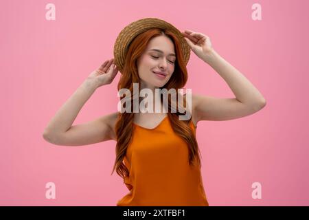Jolie jeune femme flirty dans le chapeau de paille semblant satisfait Banque D'Images