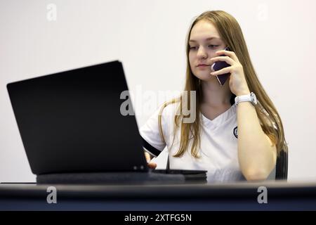 Fille avec les cheveux longs assis à l'ordinateur portable et parlant sur le téléphone portable. Concept de travail de bureau, assistant d'affaires Banque D'Images