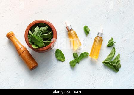 Bouteilles d'huile de menthe essentielle, mortier, pilon et feuilles vertes sur fond bleu pâle Banque D'Images