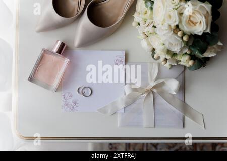 Essentiels de mariage de la mariée : talons, bouquet, bagues, parfum, et invitation sur une table blanche Banque D'Images