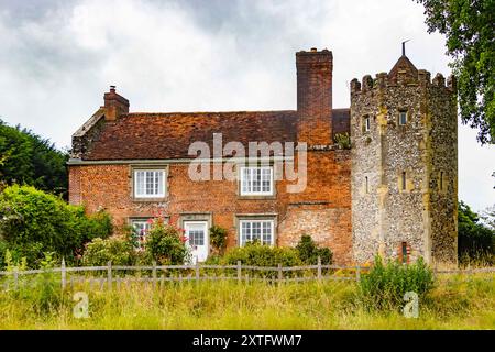 Une charmante vieille maison de campagne anglaise avec un extérieur en briques rouges, des fenêtres blanches et une tour en pierre unique, entourée d'une végétation luxuriante. Banque D'Images