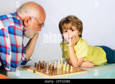 Compétition d'échecs. Enfant garçon jouer aux échecs avec grand-père. Développement cérébral et concept logique. Petit garçon pensant au prochain coup dans le jeu d'échecs. Carte Banque D'Images