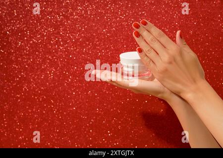 Femmes mains tenant pot cosmétique blanc sur fond rouge Banque D'Images